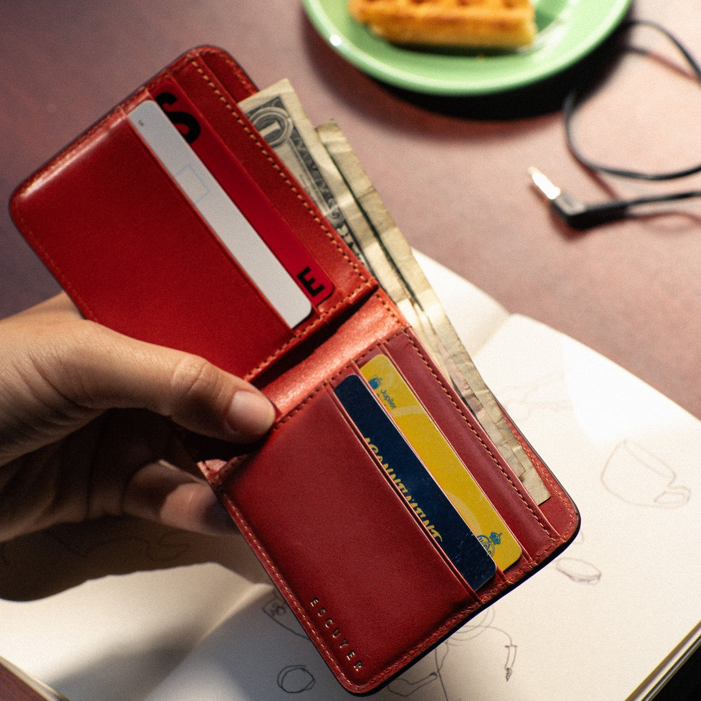Escuyer billfold wallet in light brown and orange vegetable-tanned leather, open in hand with cards and banknotes