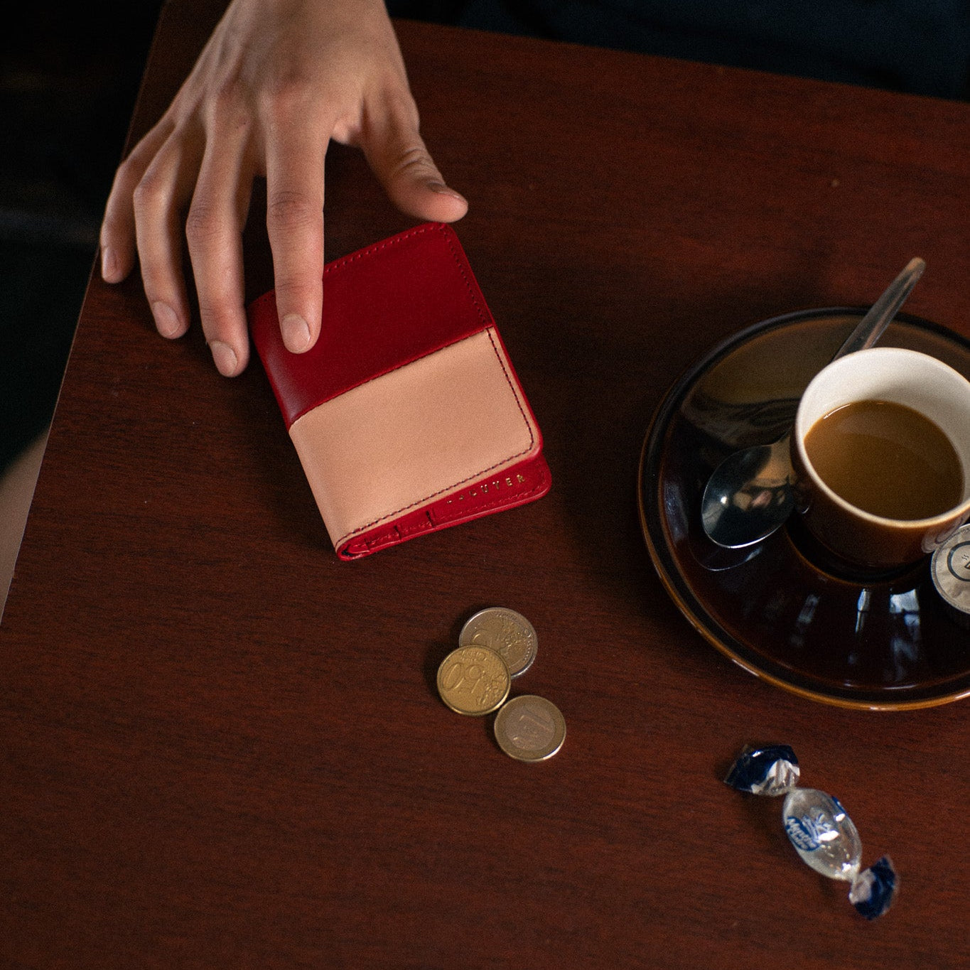 Escuyer slim wallet in red and pink vegetable-tanned leather on a café table next to a coffee and coins
