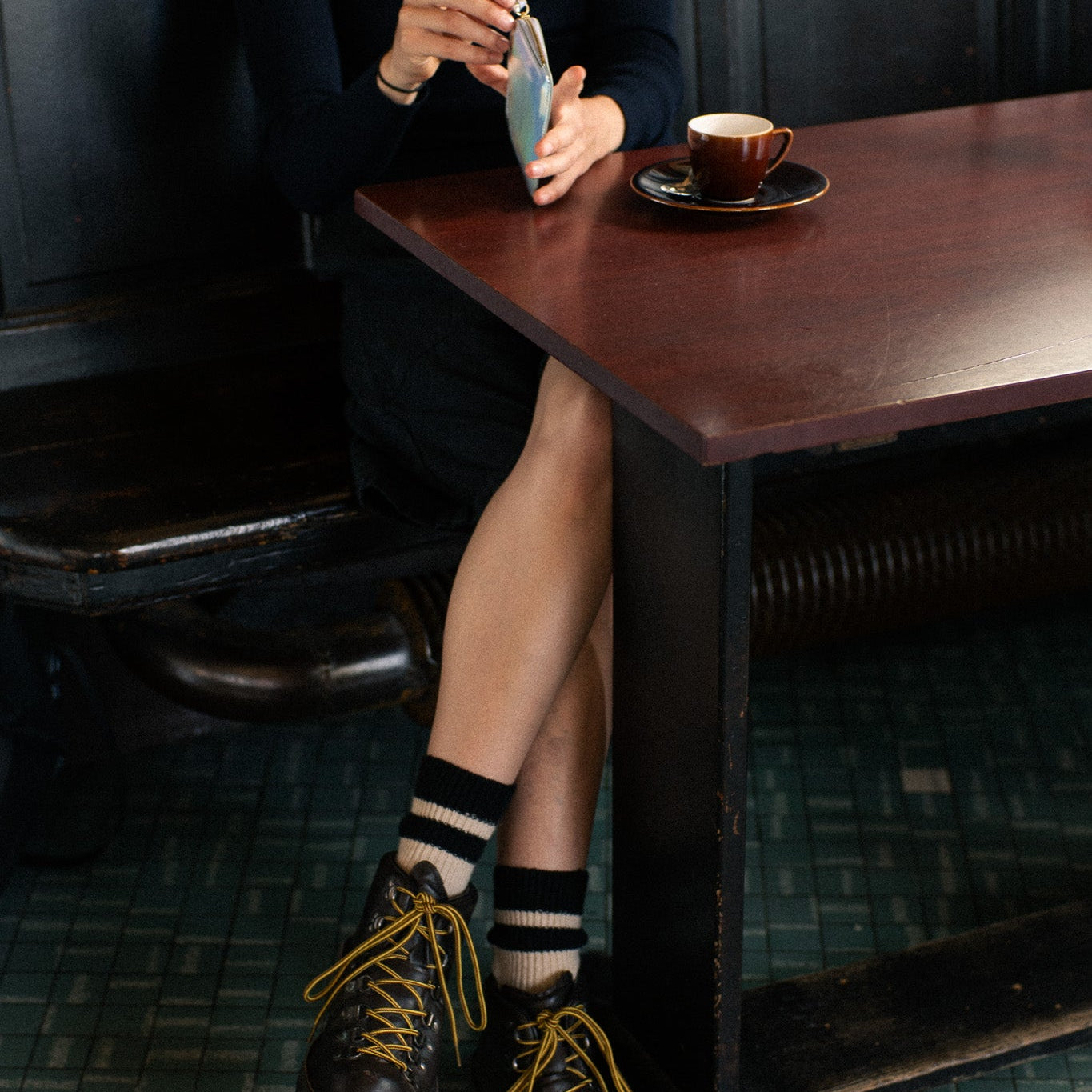 Escuyer ecru and black cashmere striped socks worn with black leather boots at a café table