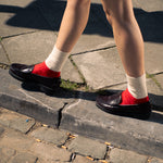 Person wearing red shoes and white socks walking on a stone pavement.