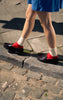 Person wearing red shoes and white socks walking on a stone pavement.