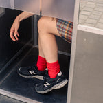 Person wearing red wool and cashmere socks from Escuyer and black sneakers from New Balance stepping out of a door.