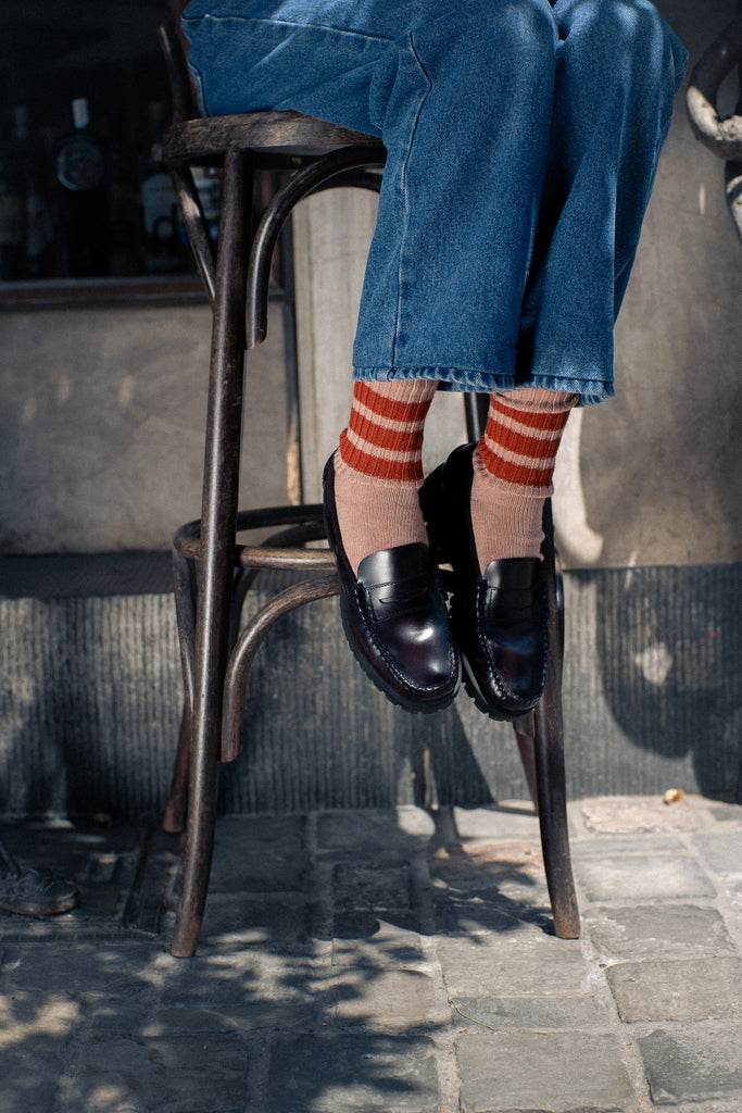 Person wearing blue jeans and striped socks sitting on a metal stool.