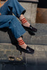 Person wearing blue jeans, black loafer shoes, and striped Escuyer socks sitting on a stone step.