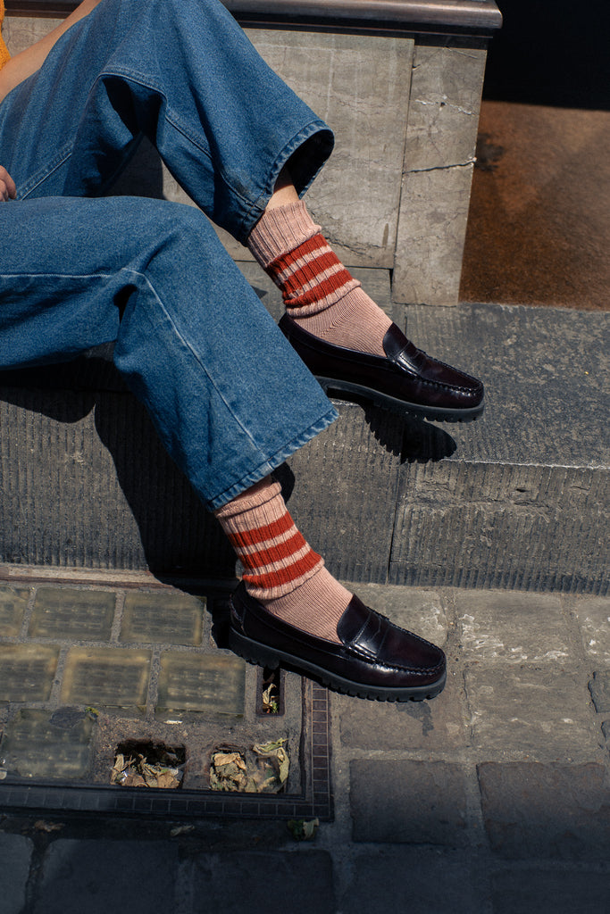 Person wearing blue jeans, black loafer shoes, and striped socks sitting on a stone step.