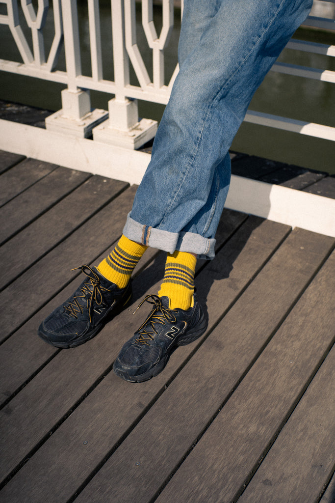 Person wearing yellow socks with rolled-up jeans and dark shoes on a wooden deck.