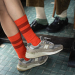 Person wearing orange striped socks and gray sneakers on a tiled floor.