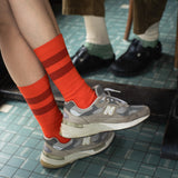 Person wearing orange striped socks and gray sneakers on a tiled floor.