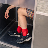 Person wearing red wool and cashmere socks from Escuyer and black sneakers from New Balance stepping out of a door.